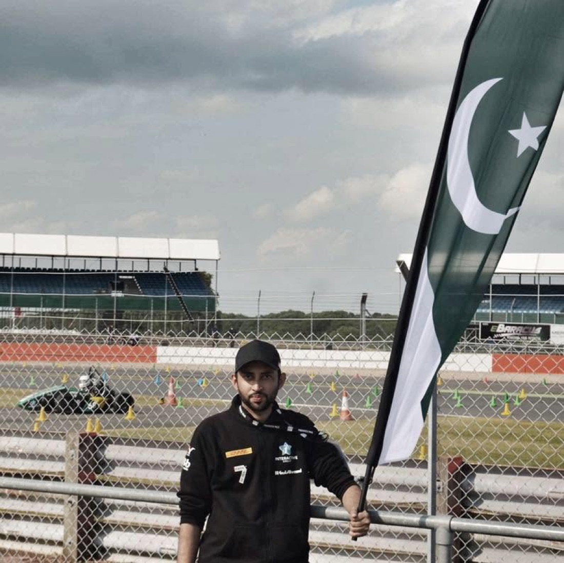 Shah Talha with the Pakistani flag, with the NUST Formula Student car behind him
